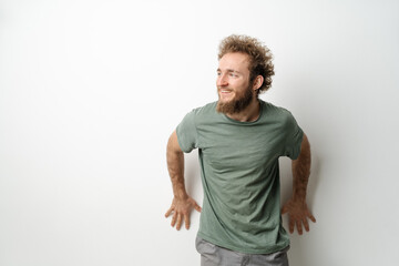 Leaned on the wall and looking sideways handsome young man with curly hair in olive t-shirt...