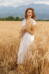 a young attractive woman in a white dress on a field of ripe cereals against the background of a blue autumn sky with clouds, the concept of harvesting, agribusiness and agriculture