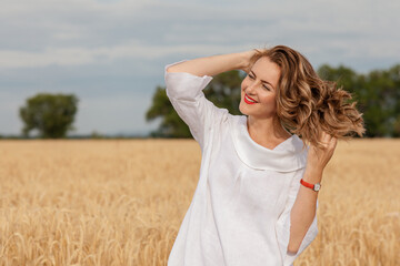 a young attractive woman in a white dress on a field of ripe cereals against the background of a blue autumn sky with clouds, the concept of harvesting, agribusiness and agriculture