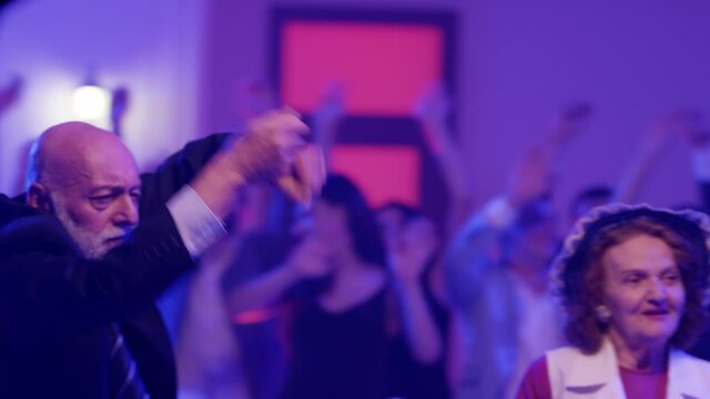 Stylish elderly couple having fun dancing at a colorful party . Sweet senior couple smiling and partying during party . Active retirement . Shot on RED HELIUM Cinema Camera	