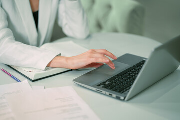No face visible Businesswoman working sitting in front of laptop wearing white official suit. Office worker female using touchpad browsing laptop while sitting at her working place. Close up. 