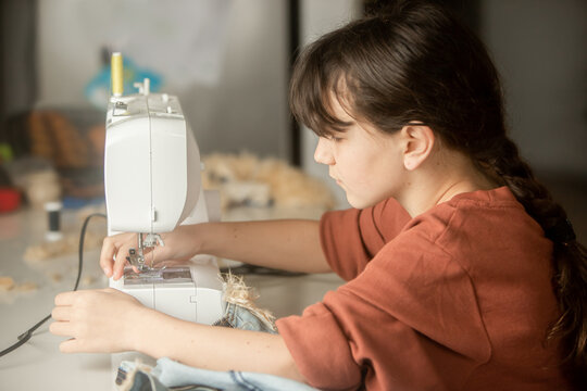 Child girl sewing at home with sewing machine