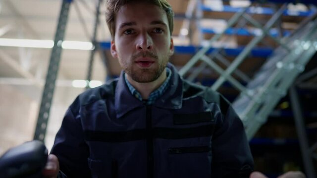 Cargo POV of young man using barcode scanner standing in industrial warehouse indoors. Portrait of concentrated serious confident Caucasian handsome man working in storage checking goods shipments