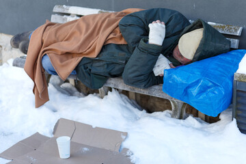 Obdachloser Mann schläfft im Winter auf einer Sitzbank - obrazy, fototapety, plakaty