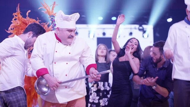 Cook and waiters dancers having fun dancing at a colorful party . Funny cook chef and waiters in white uniform, with a hat and ladle , smiling and partying during party . Cinema Camera in slow motion