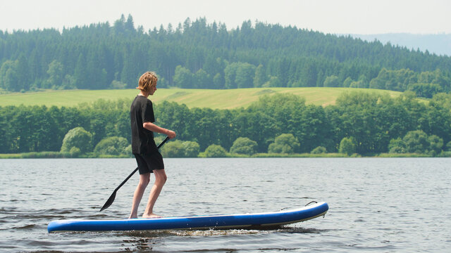 Boy rowing on stand up paddle boarding (SUP) paddling along the calm lake. The concept of children's sports and tourism.
