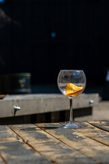Vertical photo of empty wine glass on wooden table. Unfilled cut-glass with orange slice at rustic wood table outdoors. Finished drink at open-air restaurant. 