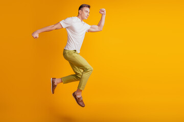 Portrait of funky positive guy jump fly run fast empty space on yellow background