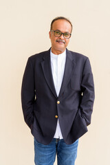 Fototapeta premium Portrait of handsome Indian businessman with mustache wearing hat against plain wall