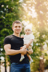 Fototapeta premium Portrait happy child boy sitting on hand of young dad, against background of green grass in park