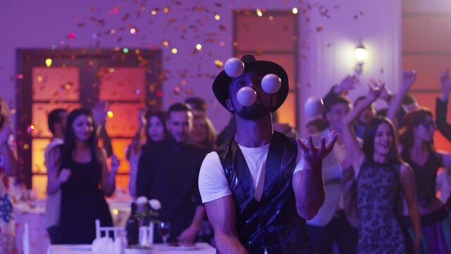 Juggler showing tricks with white balls at colorful party . Man juggling four balls at night party. Many out of focused people in the background . Shot on RED DRAGON Cinema Camera in slow motion.