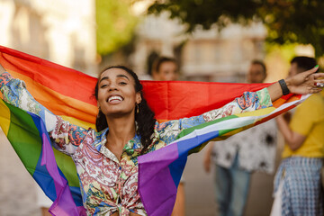 Black woman smiling and holding rainbow flag during pride parade - obrazy, fototapety, plakaty