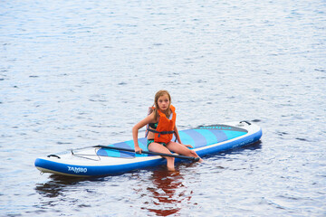 Paddle boarder. Child girl paddling on stand up paddleboard. Healthy lifestyle. Water sport, SUP surfing tour in adventure camp on active family summer beach vacation.

