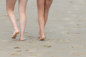 Selective focus of bare women's legs on the seashore, Low angle of two young girls or lady walking together on the sand beach with footprints, Activities and recreation in summer with friends.