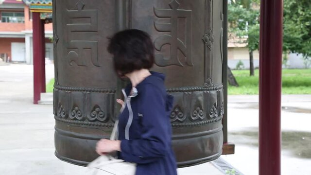 A smiling brunette in a Buddhist temple of datsan turns a drum and recites a mantra.