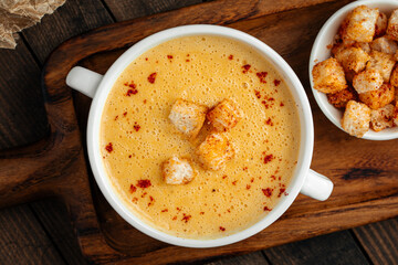 Yellow chicken cream soup with croutons in a white bowl on rustic background