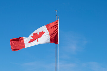 Waving Canadian flag on a post against clear blue sky with no clouds. Canada symbol - red maple leaf. Space for copy.
