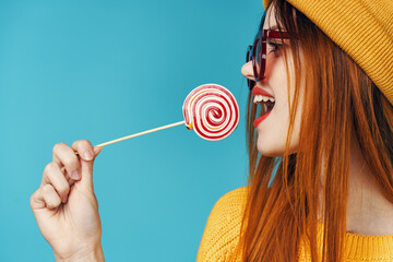 cheerful woman in a yellow sweater with a lollipop in her hands posing studio