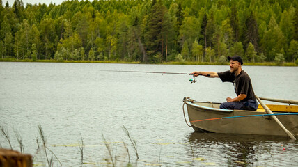 a bearded man is fishing on a spinning rod from a boat on a lake in the forest