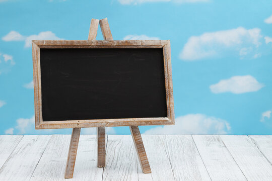 Blank standing chalkboard on weathered wood with clear sky