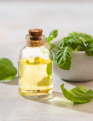 Transparent bottle of basil essential oil, fresh basil leaves in a ceramic mortar with a pestle on a light concrete background. Alternative herbal medicine and aromatherapy concept.