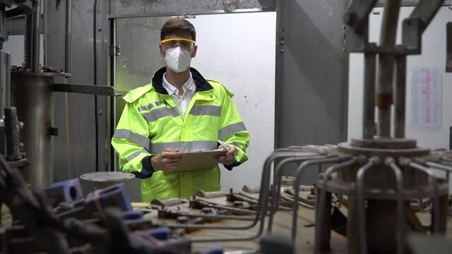 Engineer wearing face mask and protection glasses holding clipboard checking automatic machine in industry manufacturing factory. worker maintenance