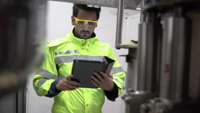 Engineer wearing protection glasses holding tablet computer  checking automatic machine in industry manufacturing factory. worker maintenance