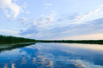 river in the morning sunrise clouds are reflected in the water reeds on the edges of the river selective focus