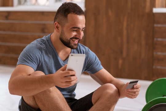 Cheerful man with smartphone and debit or credit card buying online equipment or doing sport bets and gambling online. Modern digital sports life. Sport app on smartphone. Cash app. Banking app. 
