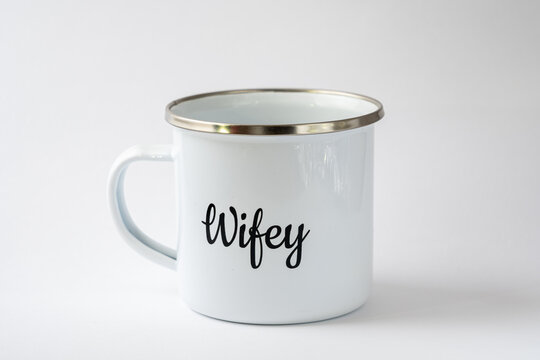 White enamel mug with a writing "Wifey" on it on a white background. Wedding accessories, cup for coffee or tea, luxury wedding.