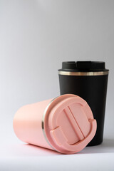 Two thermocups or thermos mugs for tea or coffee against a white background. Black and pink for him and her. Hot beverage for couples