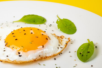 白い皿に盛りつけられた黒コショウを掛けた目玉焼きとちりばめられたベビーリーフ