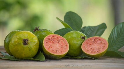 red pulp guavas on wooden table decorated with green leaves outdoors with blurred background