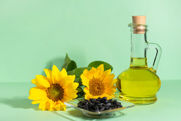 Bright yellow sunflower flowers, black seeds and a bottle of sunflower oil on a green background,...