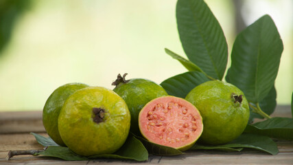 red pulp guavas on wooden table decorated with green leaves outdoors with blurred background