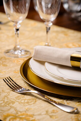 Detail of a fancy table setting with embroided tablecloth and golden sous plat