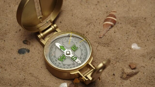 Throwing gold compass on sand background close-up, golden compass. Traveling and tourism concept, navigation.