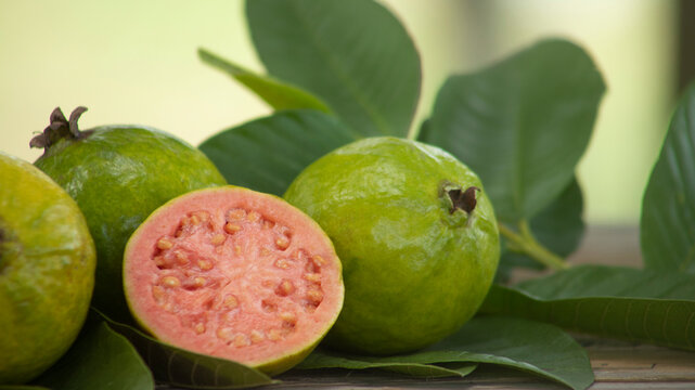 red pulp guavas on wooden table decorated with green leaves outdoors with blurred background