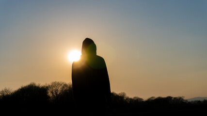 A moody, hooded figure silhouetted against the sunset. With deliberate lens flare.