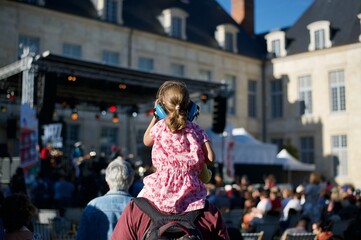 a young girl on shoulders of his father is wearing hearing protection helmet and is attending a live music show