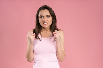 Fototapeta premium Showing ager beautiful young woman wearing pink t-shirt holding hands gathered in fists, Female half-length portrait. Human emotions, facial expression concept.