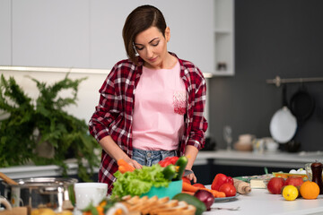 Cutting fresh vegetables pretty housewife cooking dinner wearing a plaid shirt. Cooking with passion young woman with short hair standing at modern kitchen. Healthy food leaving - concept. 