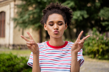 Photo of young attractive african girl pouted lips send air kiss show peace cool v-sign nature...