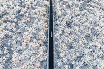 white truck driving on asphalt road along the frozen winter forest. seen from the air. Aerial view...