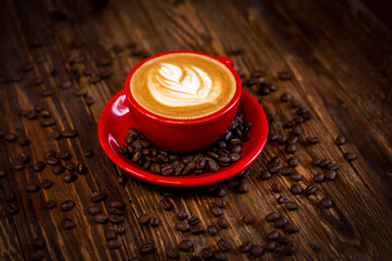 Hot cappuccino coffee in red cup with saucer on wooden table, perspective for text input..