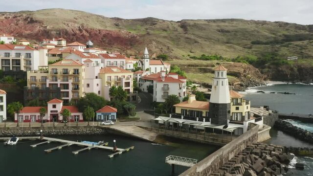 Madeira Islands, Portugal. Drone footage of the vessels floating by the coastline. Old lighthouse building with white facade, surrounded with coastal architecture. High quality 4k footage
