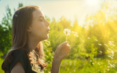 Teenage girl blowing on a dandelion in the park.
