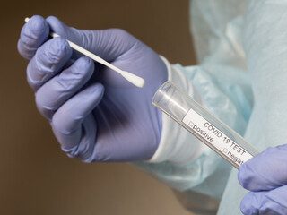 Hands in medical gloves holding an oral sample swab and a test tube for covid test