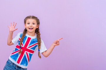 A child in a shirt with a British flag points to your ad on an isolated pink background. - obrazy, fototapety, plakaty