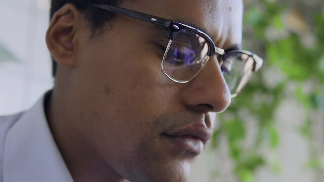 Black man freelancer working on laptop, reflection in eyeglasses, close-up face